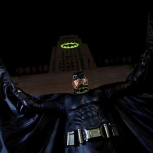 A person wearing a Batman costume poses for photos as a bat-signal is projected on City Hall in honor of late actor Adam West in Los Angeles